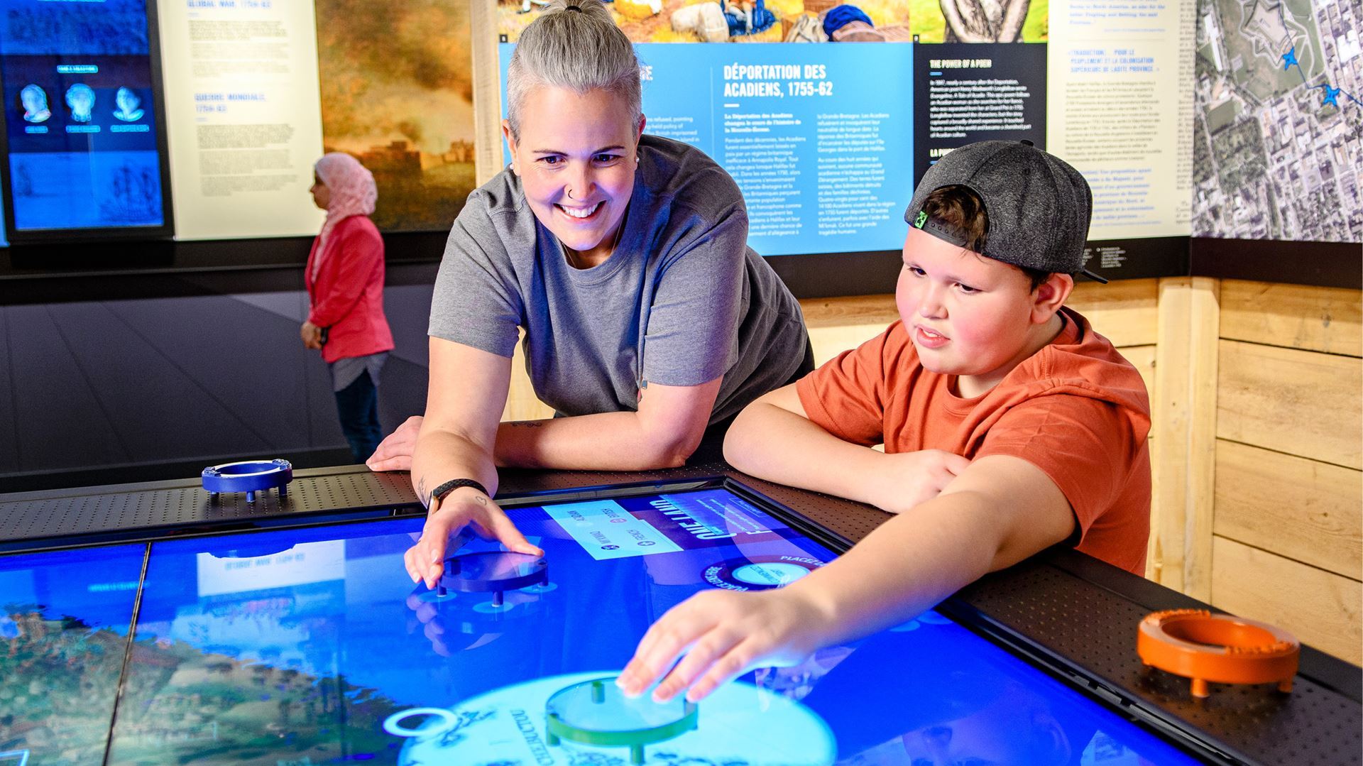 A woman and boy interact with a digital map on the illuminated surface of a table-based interactive.